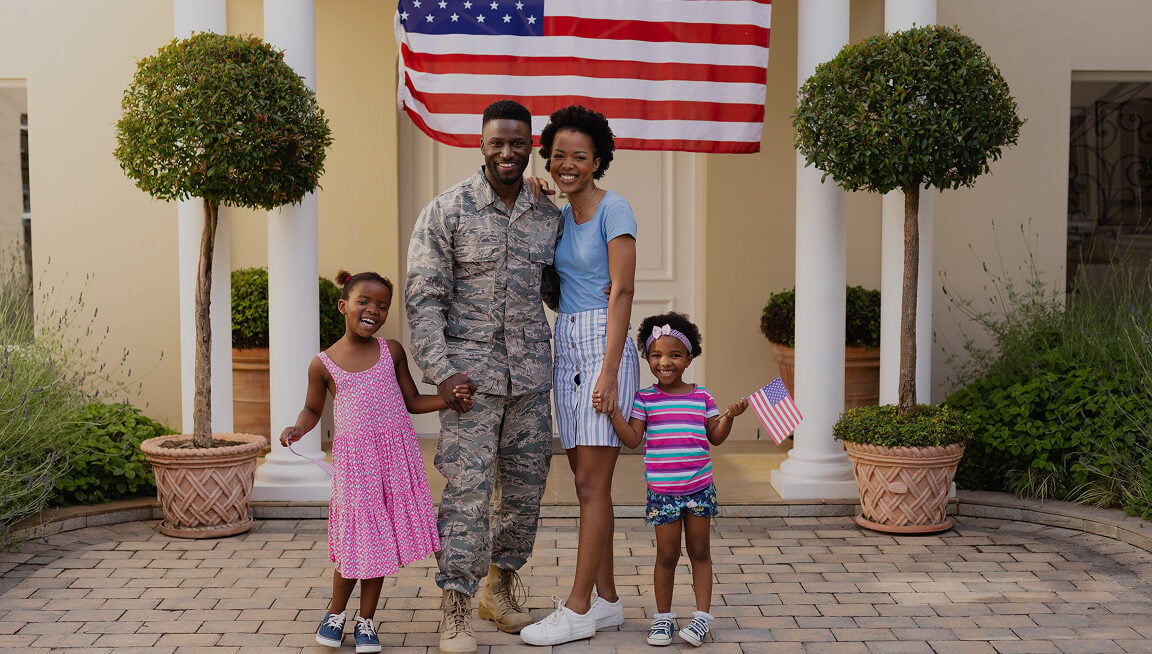 Military man with family in front of house and American flag